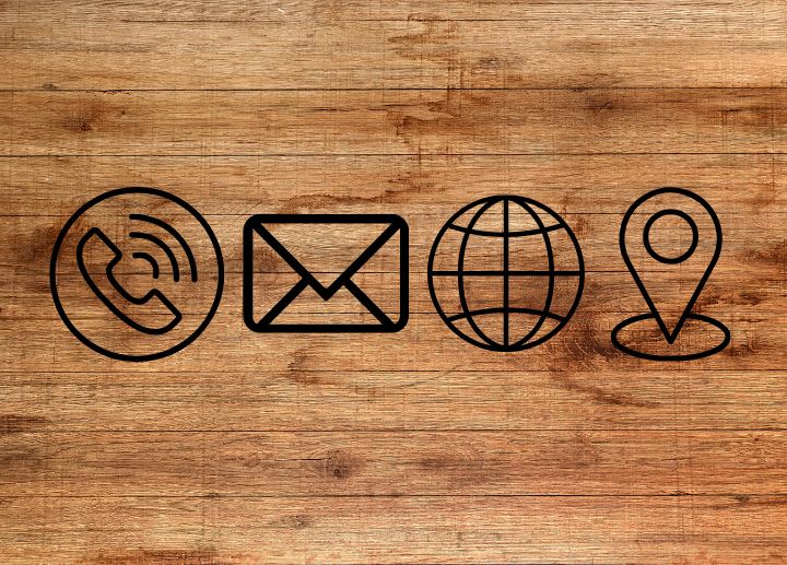 Icons of a phone, envelope, globe, and location pin on a wood background.